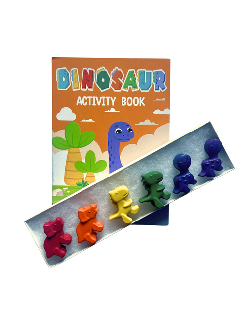 A children's activity book titled 'DINOSAUR ACTIVITY BOOK' with colorful dinosaur illustrations, shown alongside a white box holding six small dinosaur-shaped crayons in red, orange, yellow, green, blue and purple on a white background.