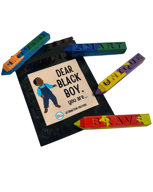 A set of colorful affirmation crayons arranged around a black book titled 'DEAR BLACK BOY, you are...' on a white background.