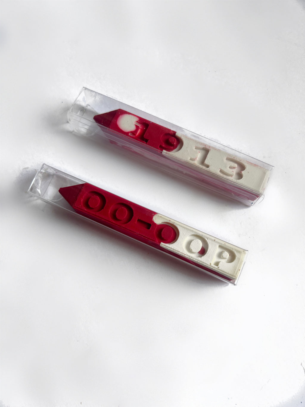 Two red and white crayons in clear plastic packaging, featuring the numbers '1913' and the letters 'OO-OOP' molded into the crayon, displayed on a clean white background.