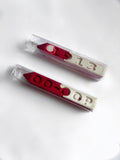 Two red and white crayons in clear plastic packaging, featuring the numbers '1913' and the letters 'OO-OOP' molded into the crayon, displayed on a clean white background.