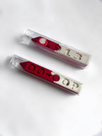 Two red and white crayons in clear plastic packaging, featuring the numbers '1913' and the letters 'OO-OOP' molded into the crayon, displayed on a clean white background.