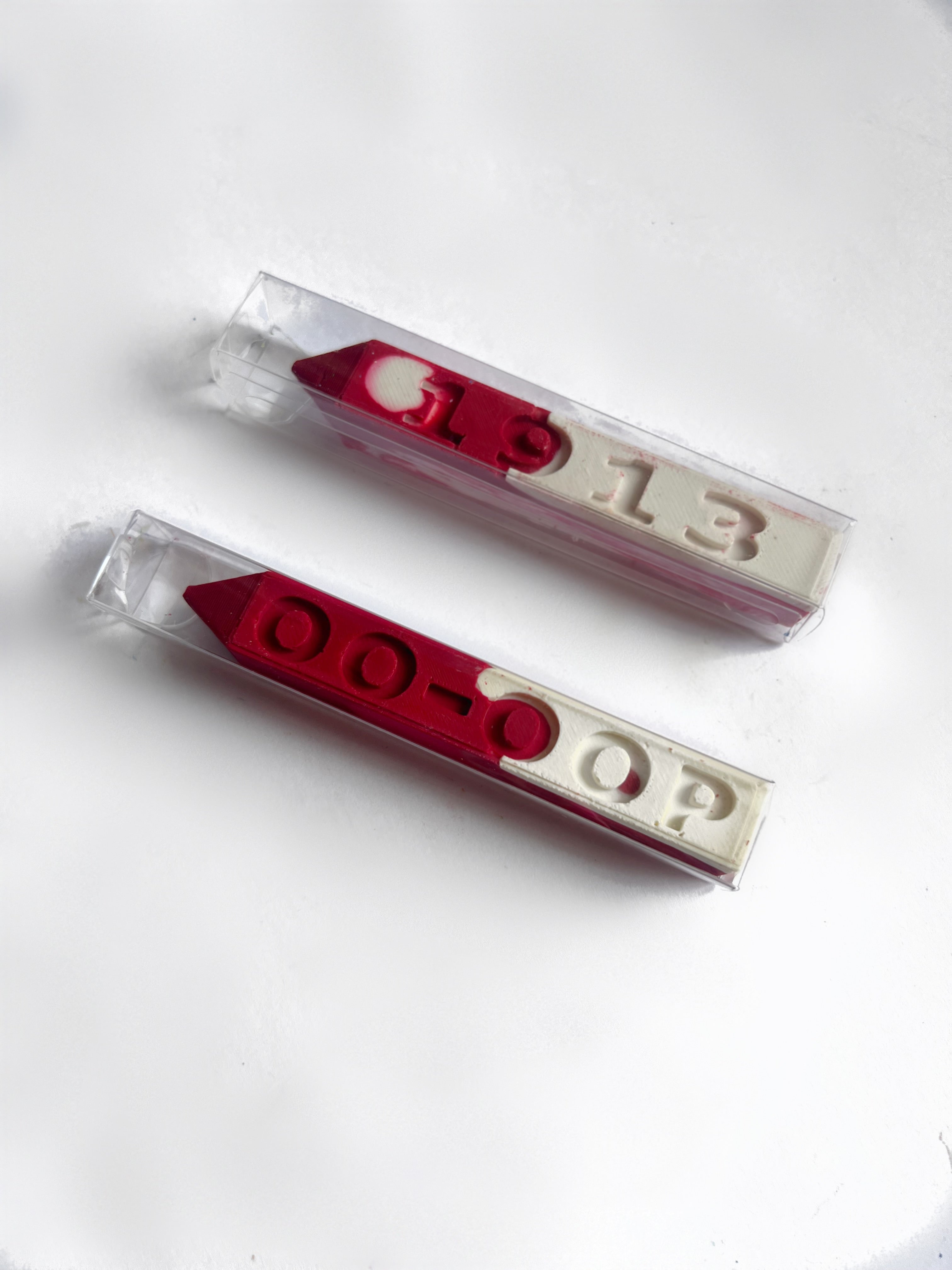 Two red and white crayons in clear plastic packaging, featuring the numbers '1913' and the letters 'OO-OOP' molded into the crayon, displayed on a clean white background.